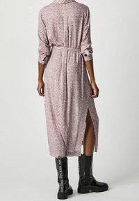 Robe longue et à motifs en rose clair et blanc, avec des manches retroussées, une taille ceinturée et des fentes sur les côtés, associée à des bottes noires jusqu'aux genoux.