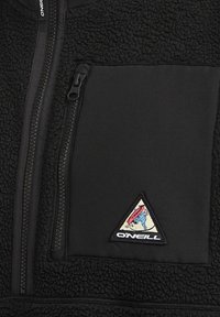 Pull en polaire noir avec une poche poitrine zippée et un patch logo triangulaire avec des graphiques multicolores, texture contrastante, matériau doux.