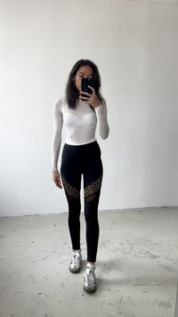 Top bianco a maniche lunghe abbinato a leggings neri con pannelli in rete a fantasia leopardata. Indossato con sneakers grigie e bianche. Ambientazione minimalista.