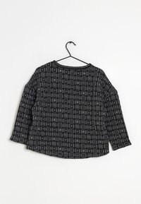 Chemise noire à manches longues avec un motif géométrique en tons de gris. Présente un col rond et une coupe décontractée. Suspendue à un cintre noir.