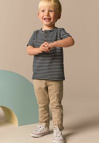 Stripet navy og hvid kortærmet T-shirt med knapdetalje, parret med beige bukser og hvide sneakers. Står foran en lys baggrund.