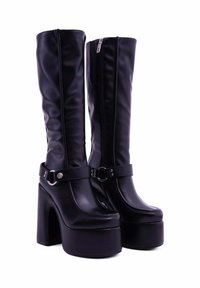 Stivali al ginocchio in finta pelle nera con tacco a piattaforma chunky, zip laterale e dettaglio con cinturino alla caviglia regolabile. Texture liscia e design elegante.