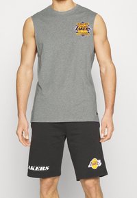 Szara bezrękawnikowa koszulka z logo Lakers na piersi, zestawiona z czarnymi szortami z napisem „LAKERS” i logo Lakers po bokach.