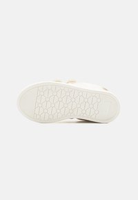 Semelle de sneaker avec une surface en caoutchouc blanc texturé, de forme plate, et un motif circulaire, avec des détails de logo en relief.