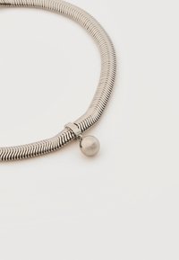 Collier chaîne serpent en argent avec un pendentif rond en argent suspendu près du fermoir sur un fond blanc.
