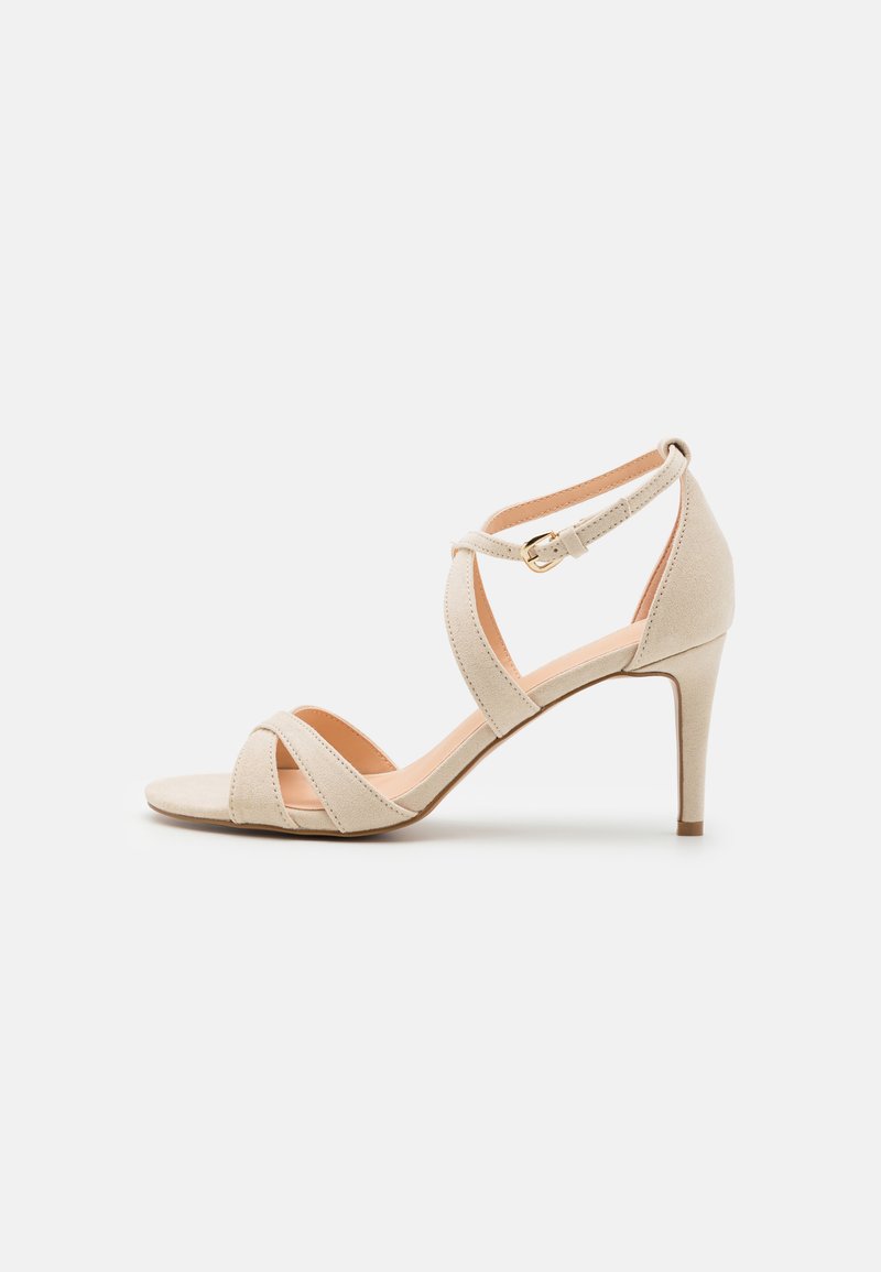 Beige suede sandaalit, joissa on korkea korko, avoin kärki, ristikkäiset hihnat ja nilkkahihna, jossa on kultainen solki.