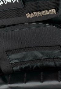 Čierna textilná taška s hladkým interiérom. Obsahuje zipsovú kapsu, suchý zips a kovový akcent s logom "Iron Maiden".