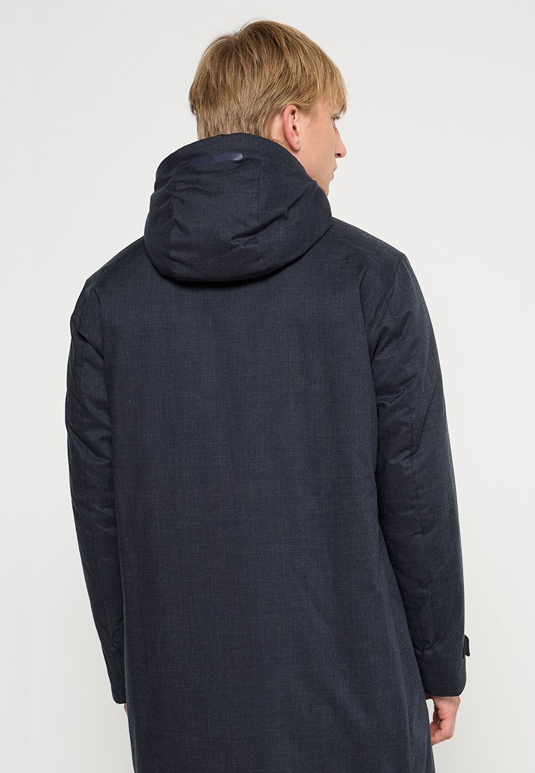 Manteau noir texturé avec une capuche, présentant une coupe droite et des manches longues. La vue de dos montre un tissu lisse et un minimum de détails.