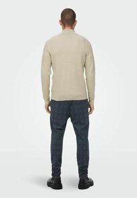 Jersey beige acanalado y pantalones de cuadros oscuros, combinados con zapatos negros. El suéter tiene un cuello alto y mangas ajustadas. Los pantalones son de corte holgado.