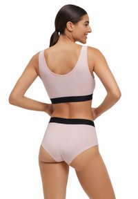 Lichtroze sportbeha en bijpassende high-waisted onderbroek met een zwarte elastische band. Glad materiaal met een aansluitend ontwerp.