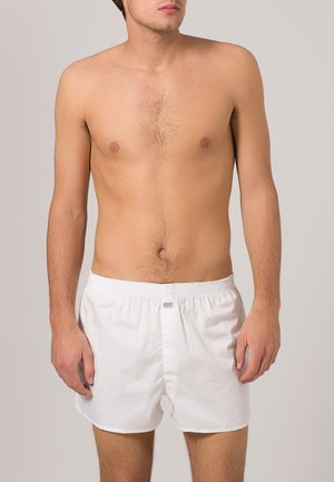 Hvide bomuldsboxershorts med elastisk talje og et lille mærke på forsiden. Designet er enkelt og uden prygl.