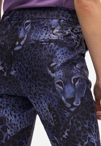 Pantaloni a vita alta in tessuto elasticizzato con un design leopardato blu, texture liscia e due tasche posteriori.