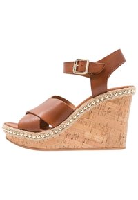 Sandalo con zeppa in pelle marrone e base in sughero, presenta una fascia con fibbia dorata e una rifinitura intrecciata con perline metalliche lungo il bordo.