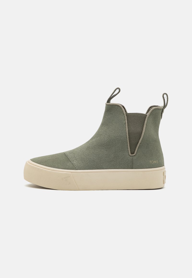 Zielone zamszowe sneakersy typu Chelsea w stylu high-top z beżową gumową podeszwą, elastycznymi bocznymi panelami, uchwytami do zakładania oraz subtelnym logo "TOMS" w pobliżu pięty.