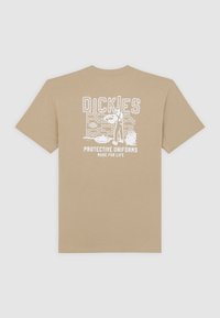 Beige cotton t-shirt featuring a white graphic print of "Dickies Protective Uniforms Made for Life" against a brick wall design. Short sleeves.