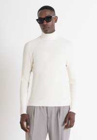 Maglione a collo alto bianco a coste con maniche lunghe e forma aderente. Presenta un tessuto testurizzato con sottili strisce verticali.
