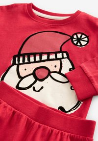 Set de pijamale din bumbac roșu, cu un grafic cu Moș Crăciun pe partea de sus, manșete cu reazem și o talie lejeră, de culoare roșie, la pantaloni.