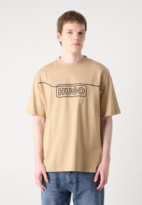 Brun bomulls T-skjorte med rund hals, med en svart omriss av "HUGO"-logoen på brystet. Korte ermer og avslappet passform.