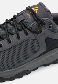 Szare buty trekkingowe z siateczkową cholewką, wzmocnionymi bokami, gumową podeszwą z przyczepnością oraz pomarańczowymi akcentami, w tym logo marki.