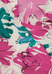 Pink and green floral blouse with a lightweight, sheer fabric, featuring button closures and a signature detail near the buttons.