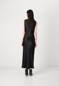 Svart satengkjole med ermeløs design, gulvlengde, glatt tekstur, med en tettsittende liv og flytende skjørt. Brukt med ankelstøvler.