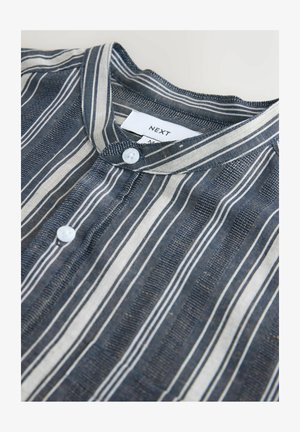 Svītraina zilā un baltā pogājamā kreklā ar apaļu apkakli un redzamu "NEXT" zīmola etiķeti kakla izgriezumā.