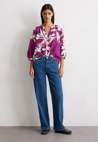 Chemise boutonnée violette avec motif floral blanc, coupe ample ; associée à un jean droit bleu taille haute et des mocassins noirs.