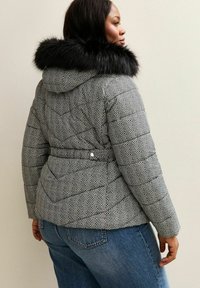 Gequilted pufferjack met een visgraatpatroon, grijs en wit, met een zwarte nepbontcapuchon. Heeft een getailleerde taille en een zachte textuur.