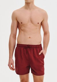 Czerwone szorty kąpielowe wykonane z lekkiego materiału, z elastycznym paskiem w talii i sznurkiem ściągającym, oraz luźnym krojem dla wygody.