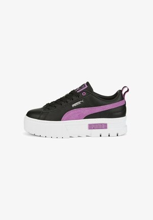 Zapatilla negra de Puma con suela blanca gruesa, detalles en raya morada, cordones y logo en el lateral y en la lengüeta trasera, vista lateral sobre fondo blanco.