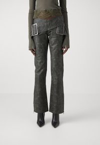 Mörkgröna läderbyxor med en lätt glans, i en utställd design, med dragkedjor vid anklarna och en texturerad yta. Bärs tillsammans med en ribbad, distressed olivfärgad topp.