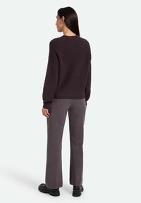 Dark purple knitted sweater with ribbed texture, paired with gray wide-leg trousers and black chunky shoes. View from the back.