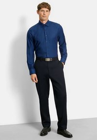 Herrenblaues Hemd mit Knopfleiste, strukturiertem Muster, langen Ärmeln und Kragen, kombiniert mit dunkler Hose und schwarzen Schuhen.