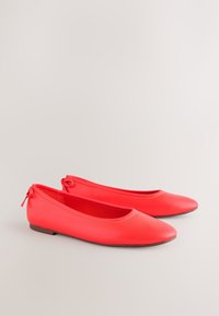 Paar leuchtend rote Ballerinas mit runden Zehen und kleinen Schlaufen hinten auf neutralem Hintergrund.