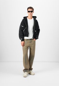 Black oversized hoodie with distressed details, white t-shirt, beige wide-leg pants, and cream-colored sneakers. Dark sunglasses complete the look.