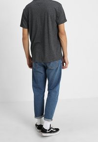 Grå kortärmad t-shirt med avslappnad passform, i kombination med ljusblå denimjeans. Svarta sneakers med vita sulor och uppvikta ärmslut.