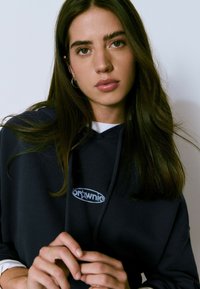 Sudadera marinera con un logo blanco que incluye una estrella, fabricada en un tejido suave, con capucha ajustable y un aspecto en capas gracias a una camisa blanca debajo.