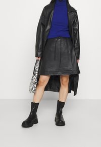 Svart läderjacka, matchande läderkjol med dragsko, blå polotröja, svarta kraftiga stövlar och en zebra-mönstrad väska.