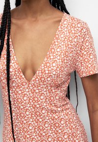 Vestido floral en naranja con estampados de margaritas blancas, con un escote en V profundo y mangas cortas, hecho de tejido ligero.