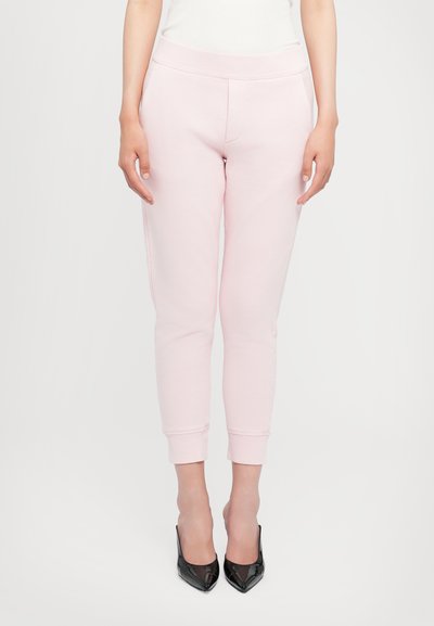 Light pink sweatpants with a smooth texture, tapered leg cuffs, and an elastic waistband, paired with black pointed-toe heels.