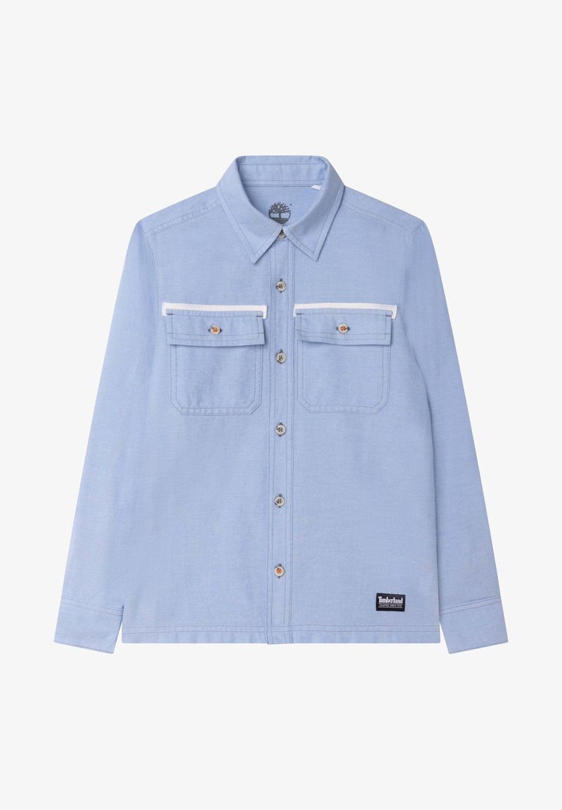 Chemise bleu clair à boutons, col pointu, deux poches poitrine à rabats et petit écusson logo Timberland près de l'ourlet.