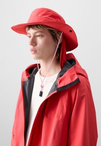 Red waterproof hat with wide brim, adjustable chin strap, and logo detail. Paired with a red jacket featuring a black inner lining.
