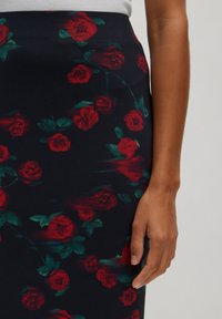 Strakke rok van zwarte stof met een bloemenpatroon van rode rozen en groene bladeren. De textuur lijkt glad en iets rekbaar.