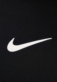 Czarna teksturowana tkanina z wyraźnym białym logo Nike w kształcie łuku. Projekt jest elegancki i minimalistyczny.