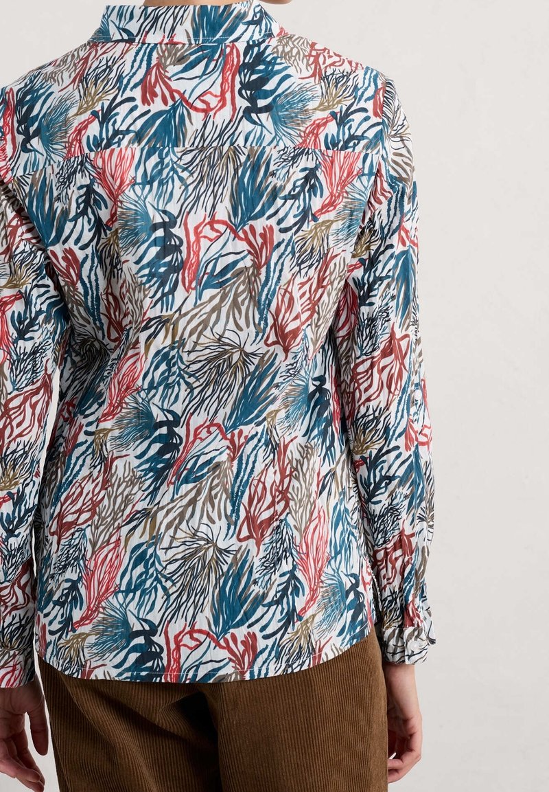 Blusa blanca con un patrón colorido de corales y algas marinas en azul, rojo y marrón. Mangas largas con puños abotonados; tejido suave y ligero.