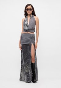 Top gris de halter con lentejuelas de un lado, combinado con una falda gray fruncida que presenta una abertura alta en el muslo. La modelo lleva botas negras hasta la rodilla.