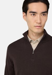 Tumši brūns džemperis ar ceturtā daļa rāvējslēdzēju, ar gludu tekstūru un vieglu dizainu, valkāts virs gaišas krāsas krekla ar apkakli.