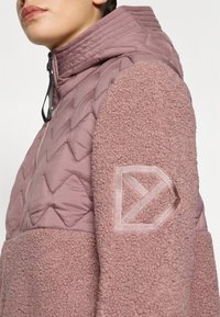 Quilted pink jacket with a plush, textured fabric on the sleeves. Features a hood and an embroidered logo on the arm.