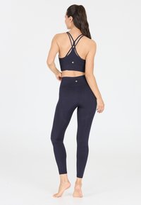 Marineblauer Sport-BH mit Kreuzträgern und strukturierten Leggings. Beide bestehen aus elastischem Stoff und verfügen auf der Rückseite über ein dezentes goldenes Emblem.