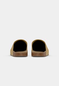 Lukkede slip-on sko med en gul semsket overdel og en brun korksåle. Glatt tekstur med rund form og åpen foran.